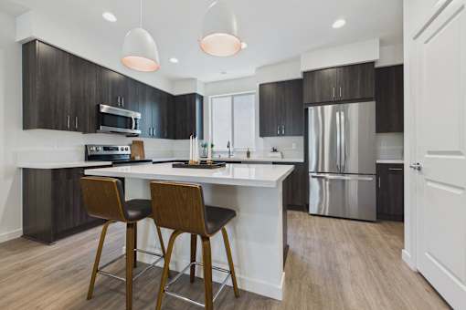 A modern kitchen with a white island and wooden chairs.