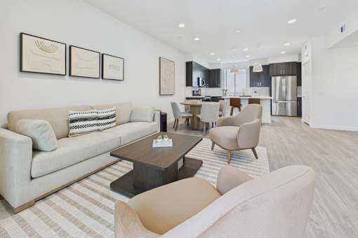 A modern living room with a beige couch, a coffee table, and a kitchen area in the background.