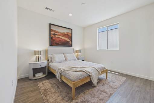 A bedroom with a bed, nightstand, and a painting on the wall.
