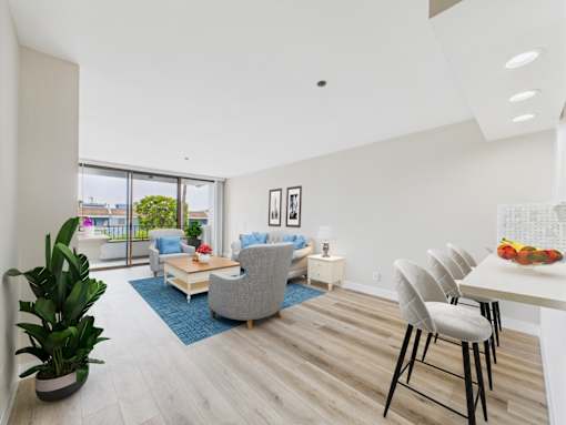 A living room with a grey couch, a blue rug, a wooden floor and a large window.