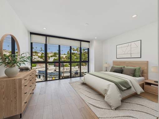 A bedroom with a large bed, a wooden dresser, and a view of the city through the windows.