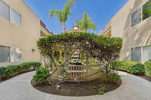 A tree-covered gazebo is in the middle of a courtyard.