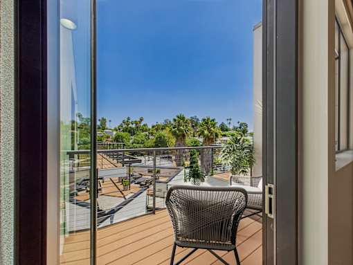 A chair is on a balcony with a view of a parking lot and trees.