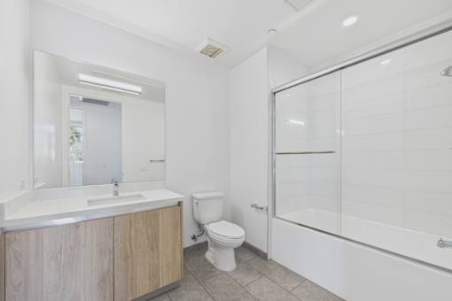 A white bathroom with a wooden vanity and a walk-in shower.