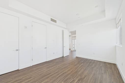 A room with white walls and wood flooring with three white doors.