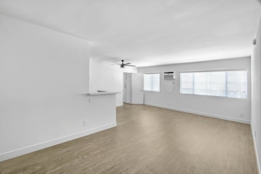 an empty living room with white walls and wood flooring and a ceiling fan