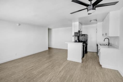 an empty living room with a kitchen and a ceiling fan