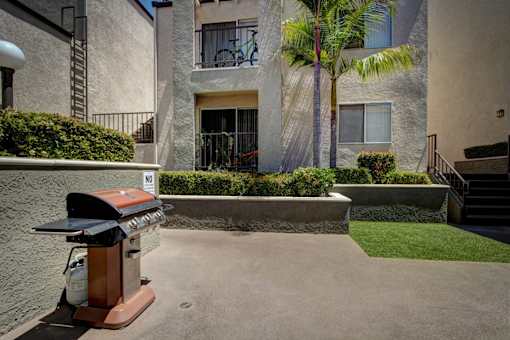 A small patio with a grill and a building in the background.