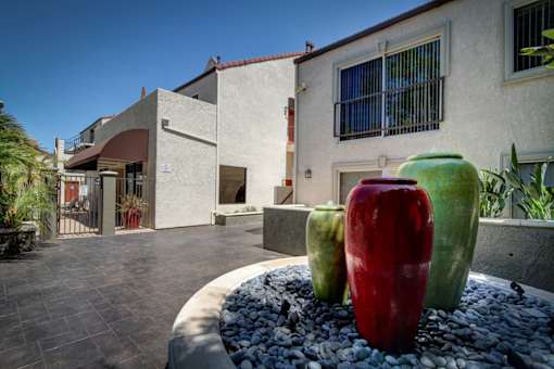 A red vase sits in front of a building with a grey vase and a green vase beside it.