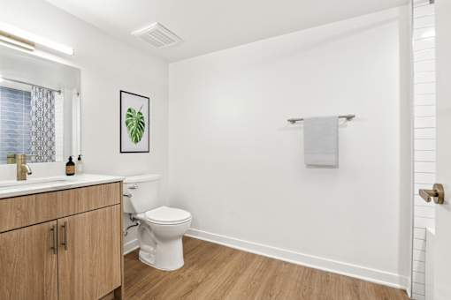A white bathroom with a toilet, sink, and a picture of a leaf on the wall.