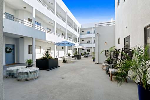 A sunny day at the courtyard of a white building with blue umbrellas and potted plants.