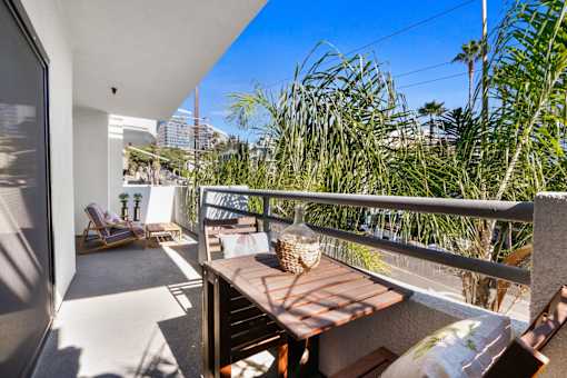A balcony with a table and chairs overlooks a lush green area.