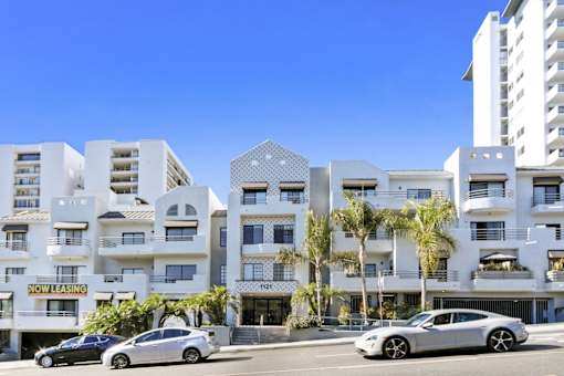 A modern apartment complex with a "Now Leasing" sign in front of it.