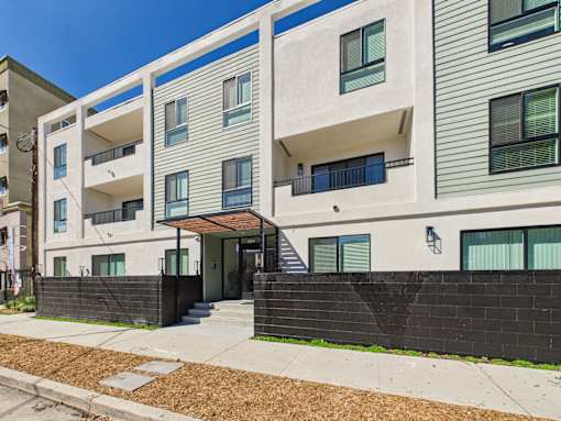 A modern apartment building with a black fence and a clear blue sky.