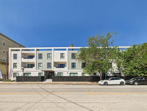 A white and grey apartment building with a tree in front of it.