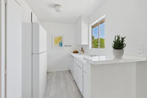 A white kitchen with a fridge, sink, and a window.