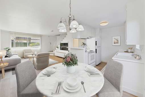 A modern dining room with a table set for two and a kitchen area in the background.