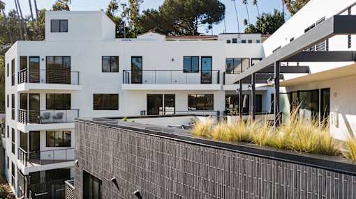 A modern white building with black balconies and a black wall in front.