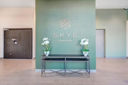 a lobby with a table and flowers in front of a green wall