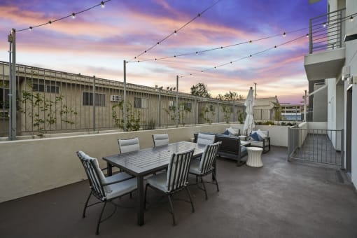 a patio with a table and chairs and a sunset in the background