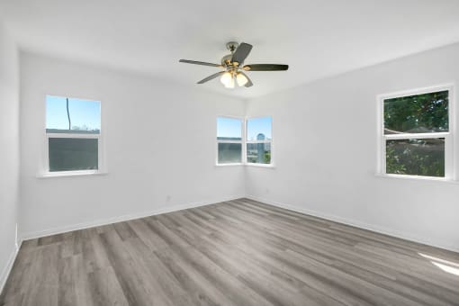an empty living room with a ceiling fan and three windows