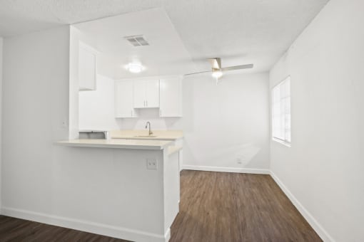 an empty living room and kitchen with white cabinets and wood flooring