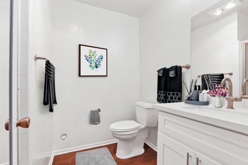 a bathroom with white walls and wood floors and a white toilet next to a sink with a