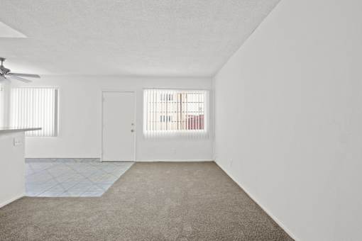 the living room and kitchen of an apartment with white walls and carpet