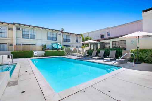 a swimming pool with lounge chairs and umbrellas in front of a building