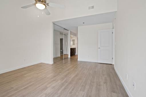 A room with a ceiling fan and light fixture, and a door leading to another room.