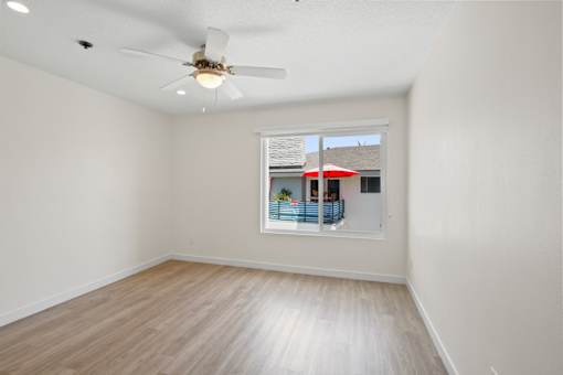 A room with a ceiling fan and a window showing a red umbrella outside.