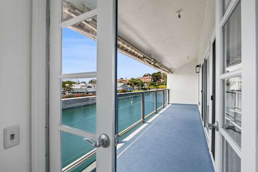 A white door opens to a balcony with a view of a body of water.