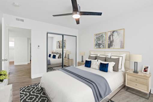 A bedroom with a large bed, a ceiling fan, and a mirror on the wall.
