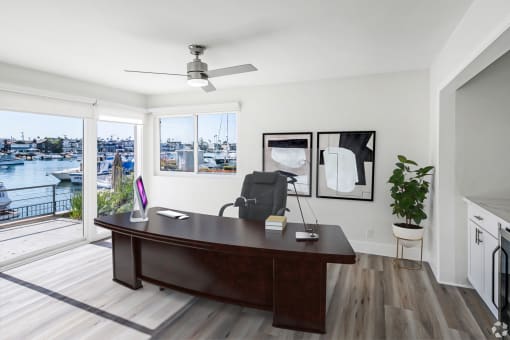 a home office with a large wooden desk and a sliding glass door that leads to a deck