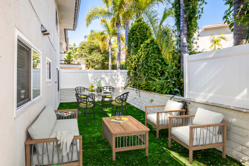 a patio with a wooden table and chairs and a white fence