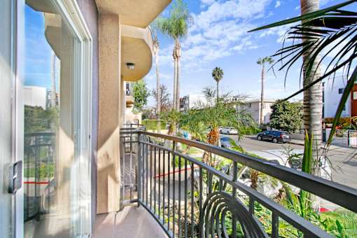 A balcony with a metal railing and a view of a street with cars and palm trees.