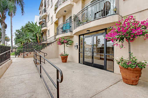 A building entrance with a black railing and potted plants.