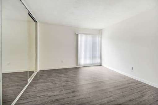 an empty living room with a mirrored wall and wood flooring