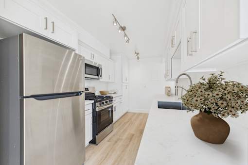 A modern kitchen with a stainless steel refrigerator and wooden flooring.