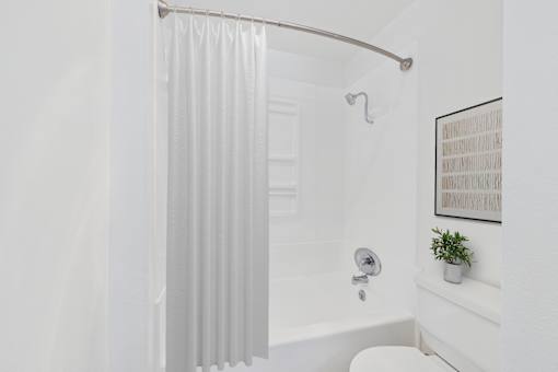 A white bathroom with a white tub and a white shower curtain.