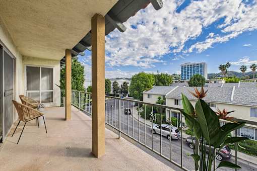 A balcony with a chair and a table is overlooking a street.