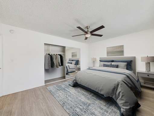 A bedroom with a bed, a ceiling fan, and a closet with clothes.