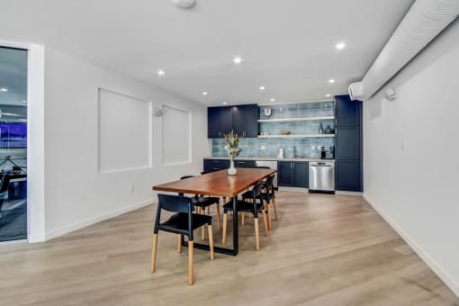 a dining area with a wooden table and chairs and a kitchen in the background