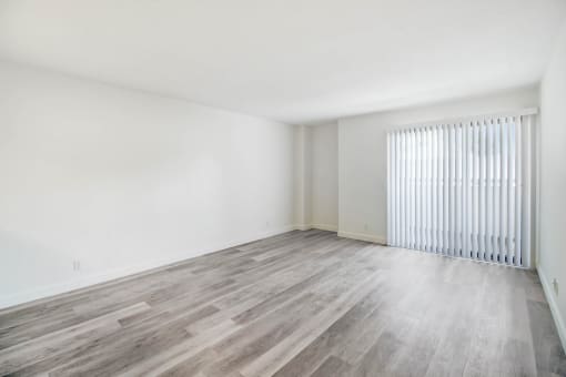the living room of an apartment with wood flooring and a large window