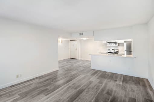 the living room and kitchen of an apartment with white walls and wood flooring