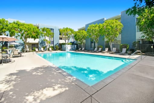 a swimming pool in front of a building with chairs and trees