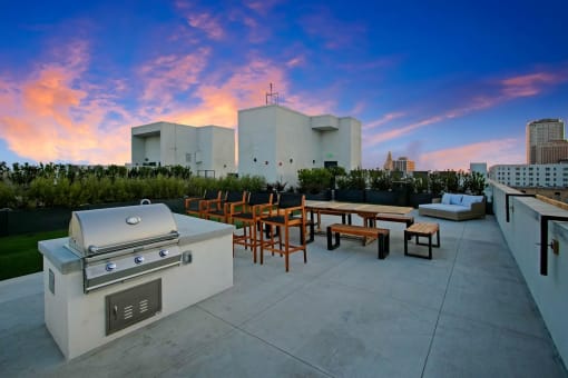 a rooftop patio with a grill and tables and a city in the background