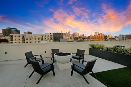 a rooftop patio with chairs and a fire pit with the city skyline in the background