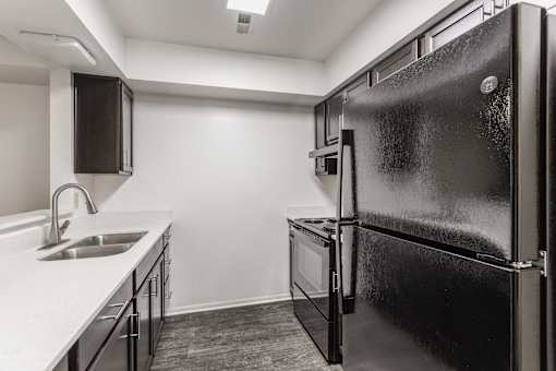 A black refrigerator is in the corner of a kitchen.