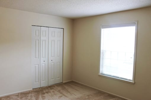 Carpeted bedroom with a window and closet at Cambridge Square Apartments Fort Wayne.